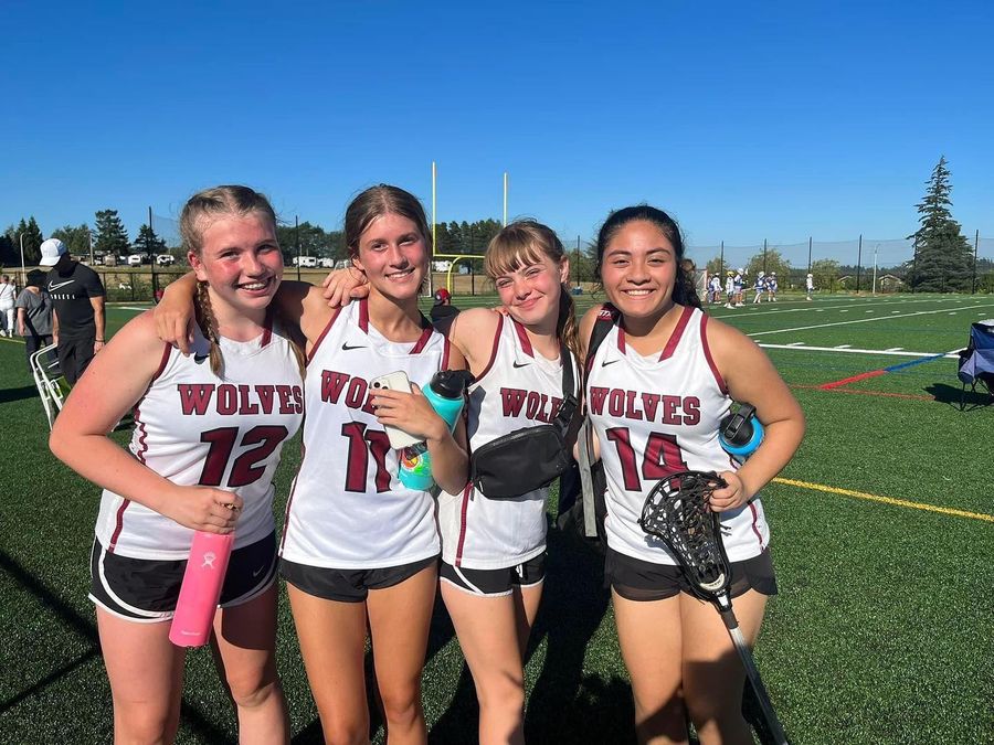 Four Tualatin girls lacrosse players smiling together on the field